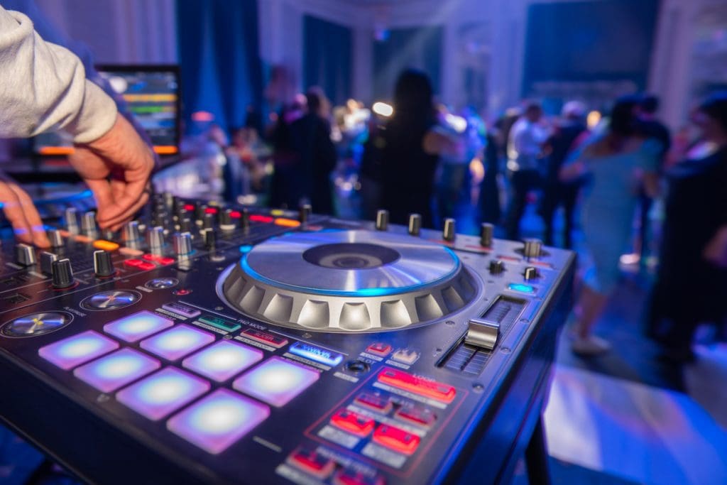 Close-up of a professional Wedding DJ at a wedding reception with lighting and guests dancing in the background