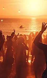 Wedding guests dancing on a beach at sunset with golden light and chilled Ibiza vibes.