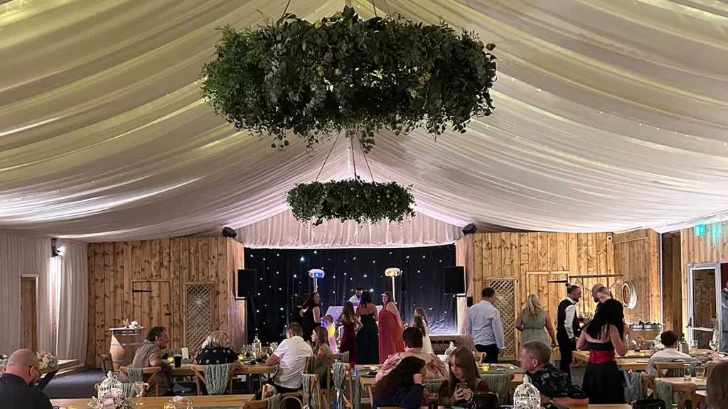 Wedding reception at Plum Park Manor with draped marquee ceiling, floral chandeliers, and rustic wooden interior.