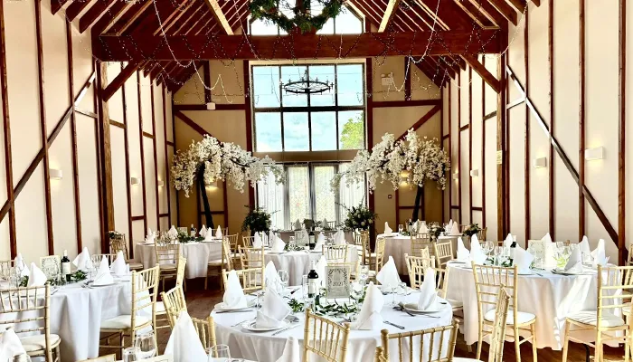 Beautiful wedding reception at Winter’s Tale Barn in Buckinghamshire with white floral décor, round tables, and golden chairs under rustic wooden beams.