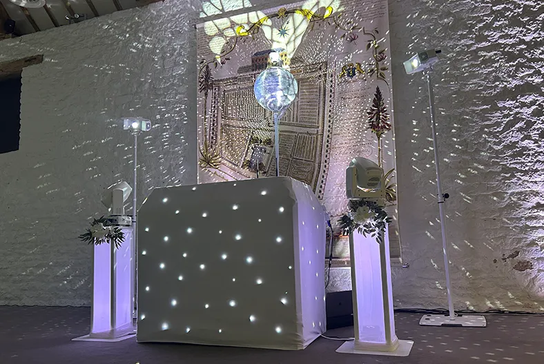Oxford Wedding DJ setup with white starlit DJ booth, mirror ball and uplighting by AURA Wedding DJs at an Oxfordshire wedding venue.