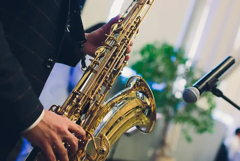 Wedding saxophonist playing golden saxophone next to a DJ microphone during a wedding performance.